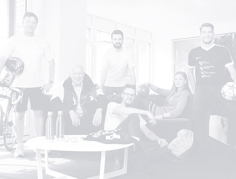 Schwarz-Weiß-Bild, das sechs Menschen mit Sportgegenständen zeigt, die auf und neben einer Couch sitzen und stehen